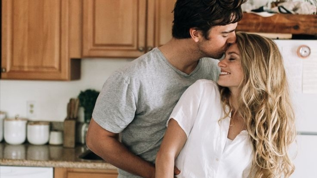 A happy, married couple is embracing in the kitchen.